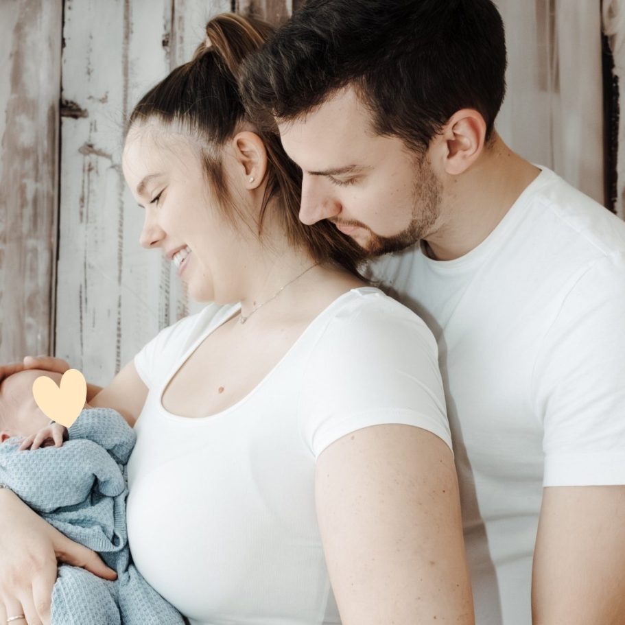 Junge Familie mit Neugeborenem, lächelnd und liebevoll umarmend. Babyfotoshooting Berlin.