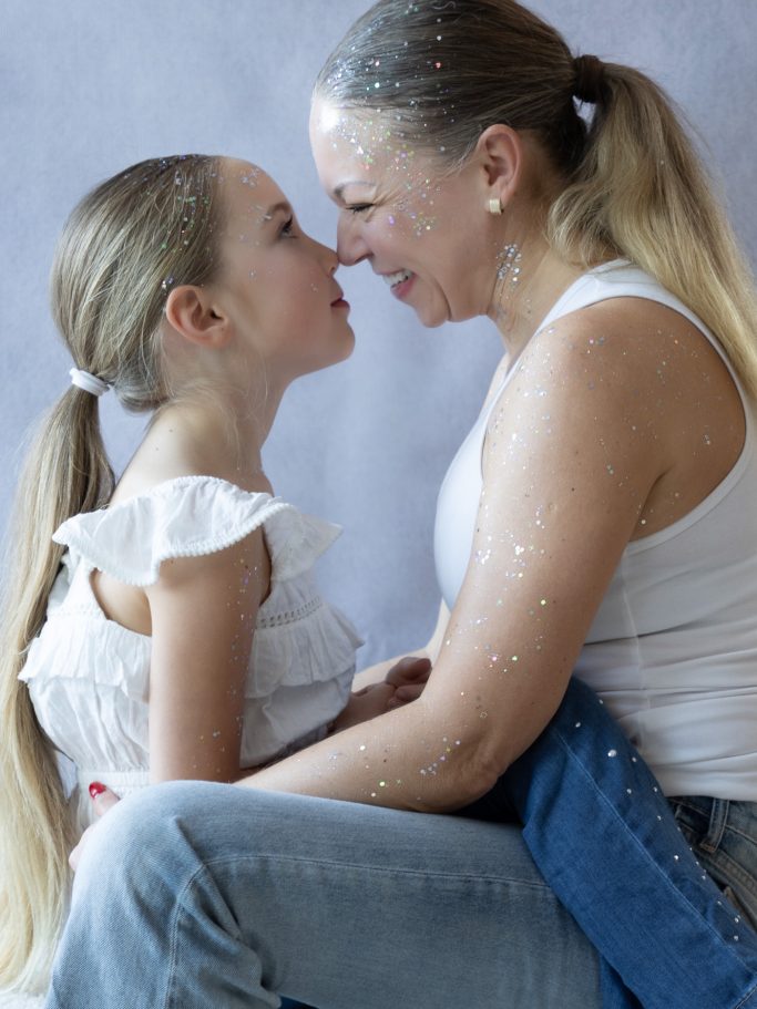 Eine lächelnde Mutter sitzt mit ihrer Tochter und blickt sich liebevoll in die Augen.