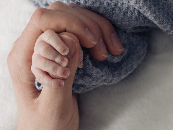 Eine erwachsene Hand hält die Hand eines Kleinkindes, eingehüllt in eine weiche Decke.