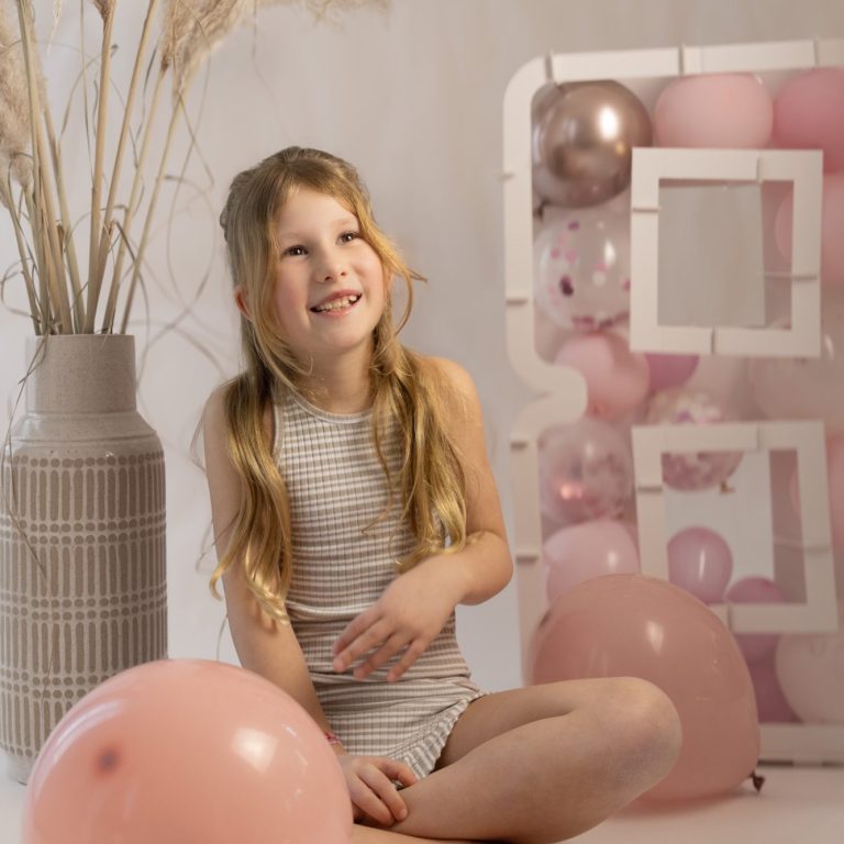 Kita- und Schulfotografie Ein Mädchen mit Blumenkranz und einem lächelnden Gesicht in einem Boho Hintergrund.