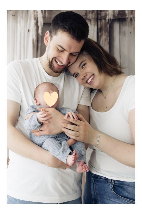 Junge Familie lächelt glücklich mit ihrem Baby in den Händen.