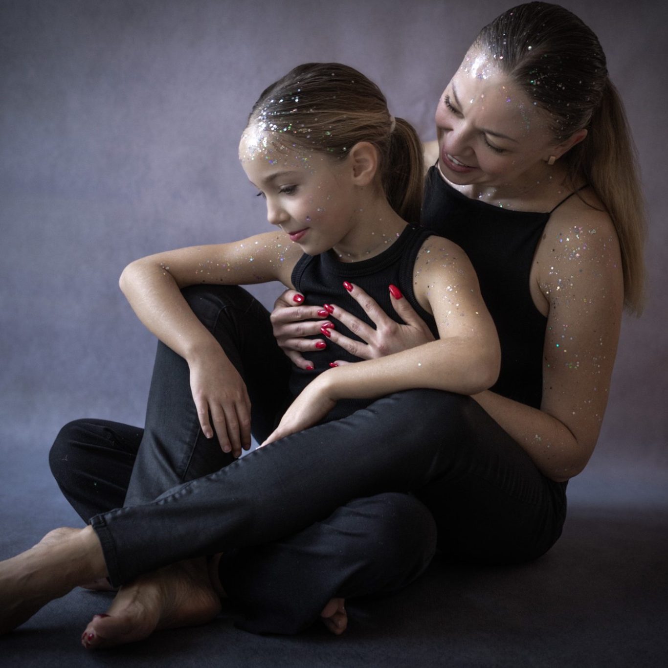 Eine Frau sitzt mit einem Kind im Schoß, beide in schwarzer Kleidung, in liebevollem Moment. Familienfotografie.