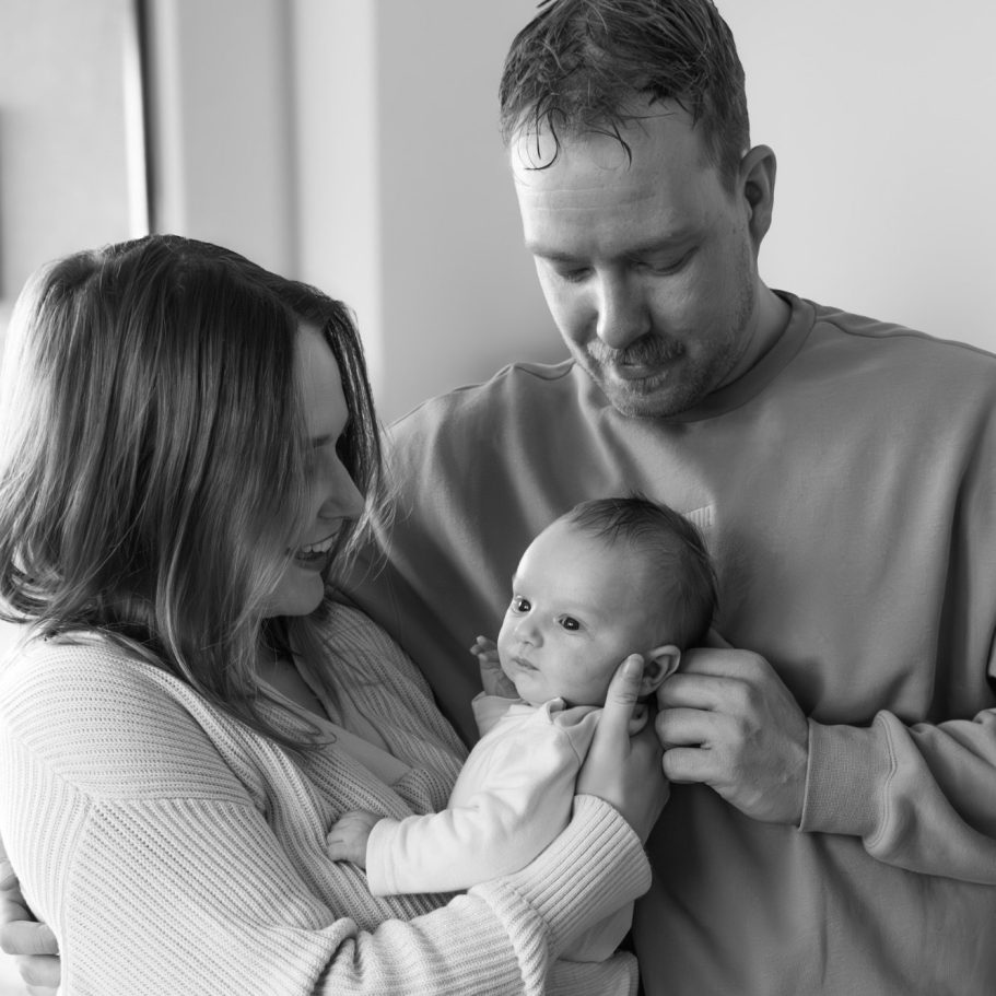 Ein Elternpaar hält ihr Baby, während sie liebevoll miteinander interagieren.