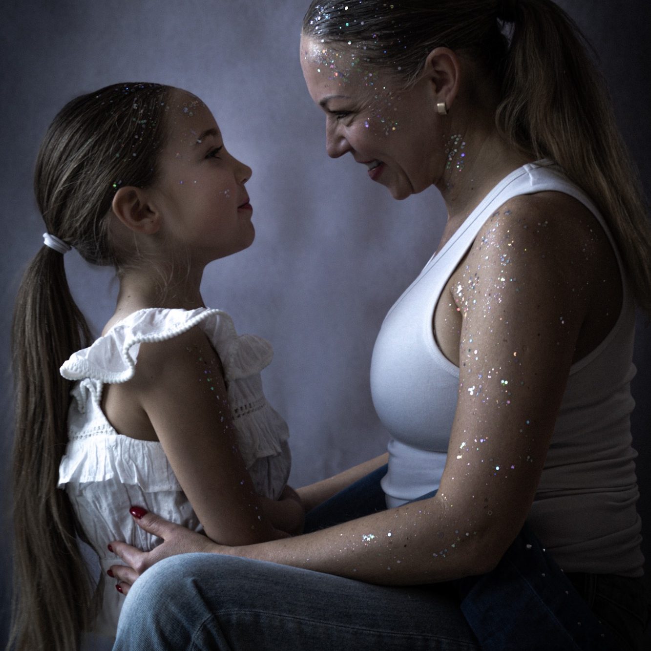 Eine Mutter und ihre Tochter blicken sich lächelnd in die Augen, beide mit Glitzer.